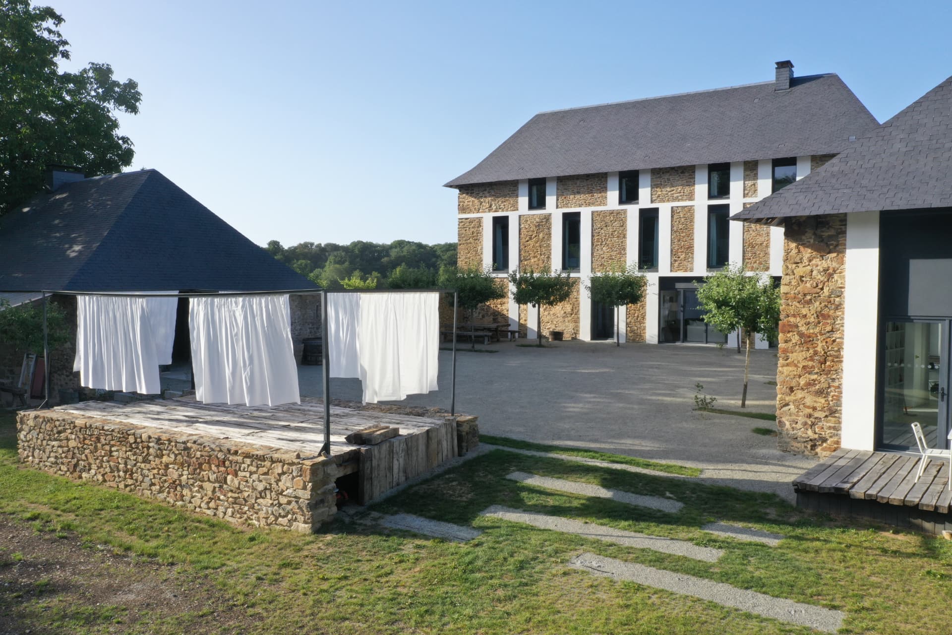 Cour de la blanchisserie réhabilitée avec ses bâtiments en pierre et ses toiles blanches au vent